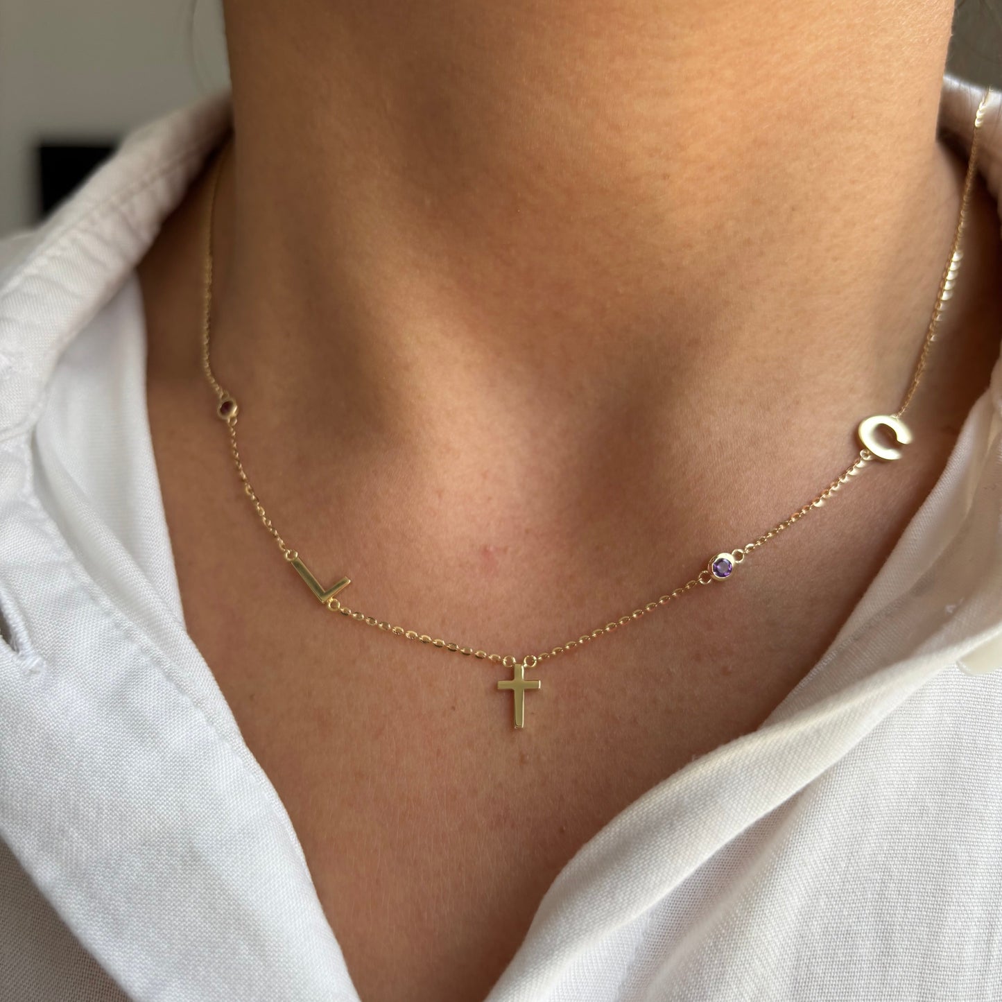 Yellow gold initial necklace with cross and coloured birthstones, worn on a model.
