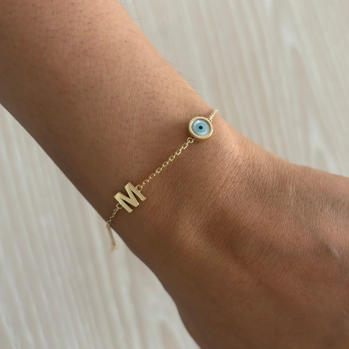 Gold bracelet with a blue eye charm on a wrist against a light background