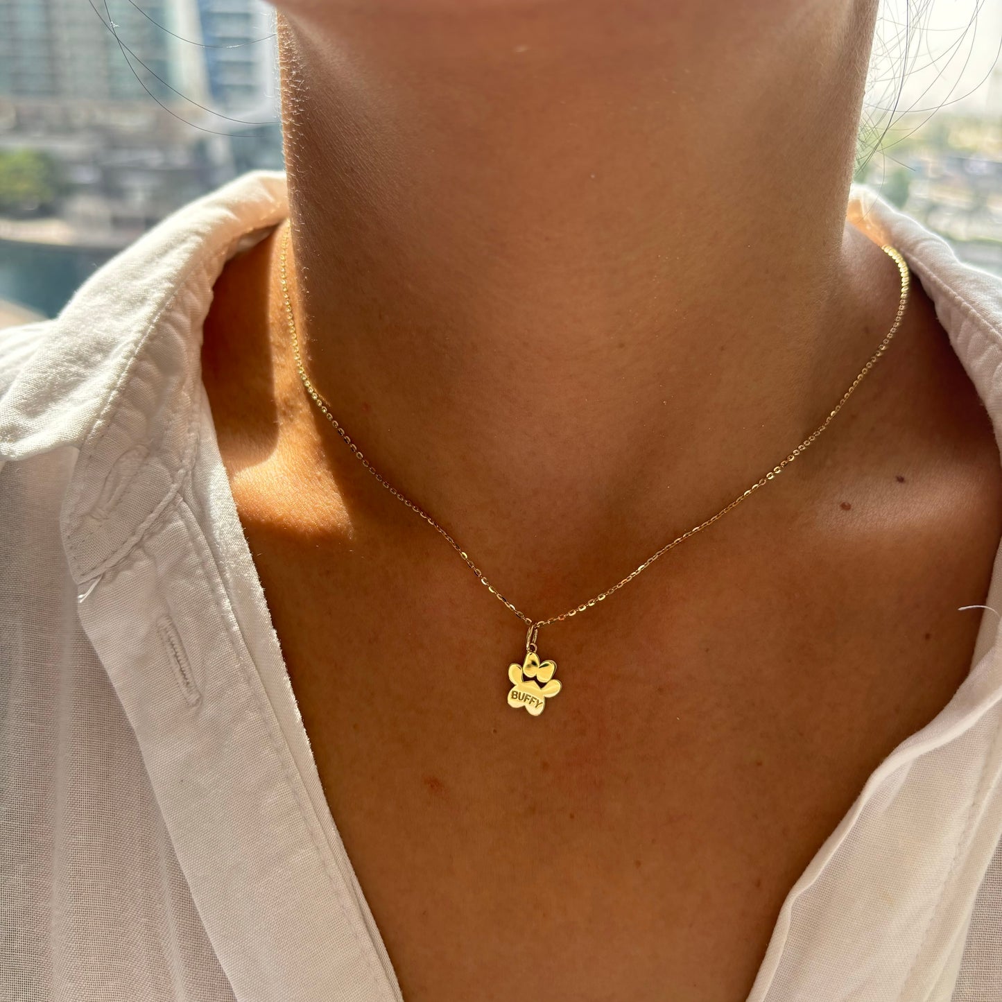 Image of a paw print shaped pendant on a gold chain on a model