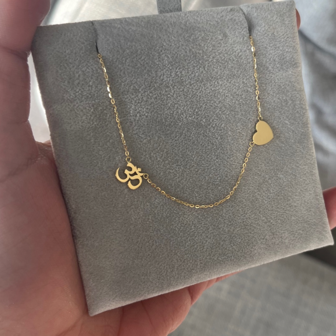 18K yellow gold two-charm necklace with Om and heart charms on a grey display card