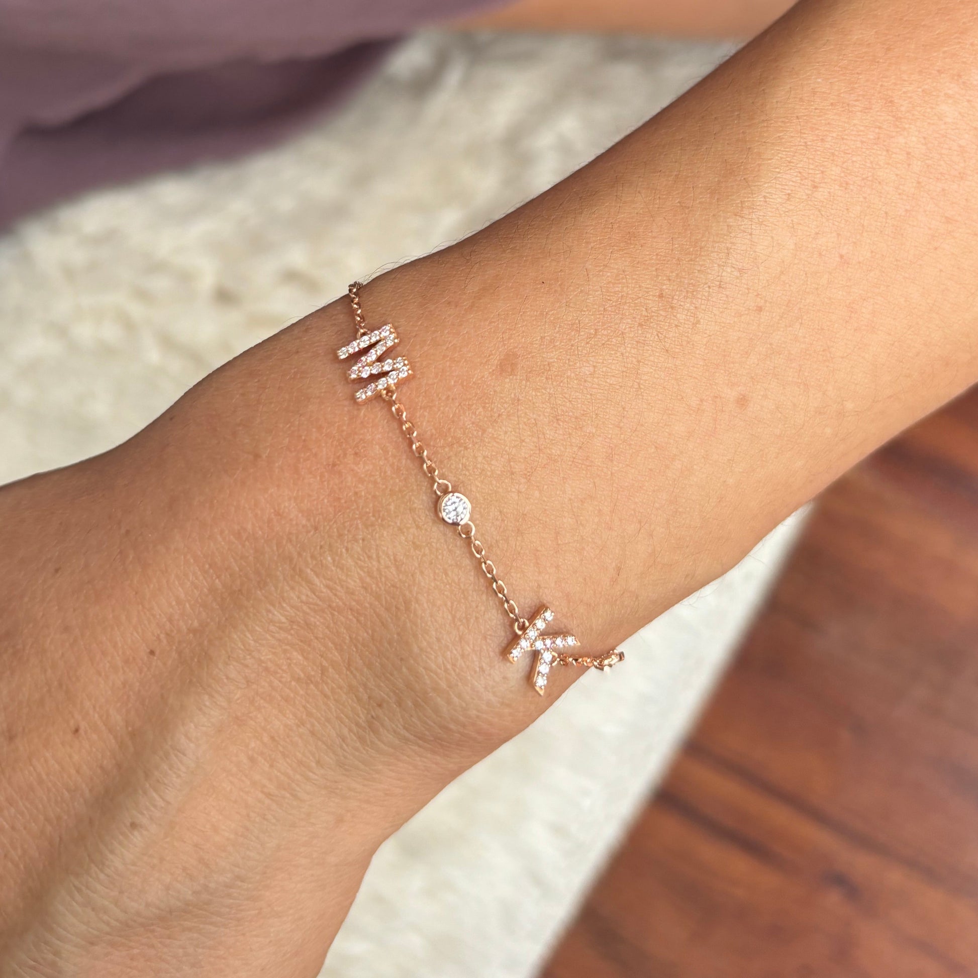 Close-up of a wrist wearing a rose gold bracelet with a letter 'M' charm.