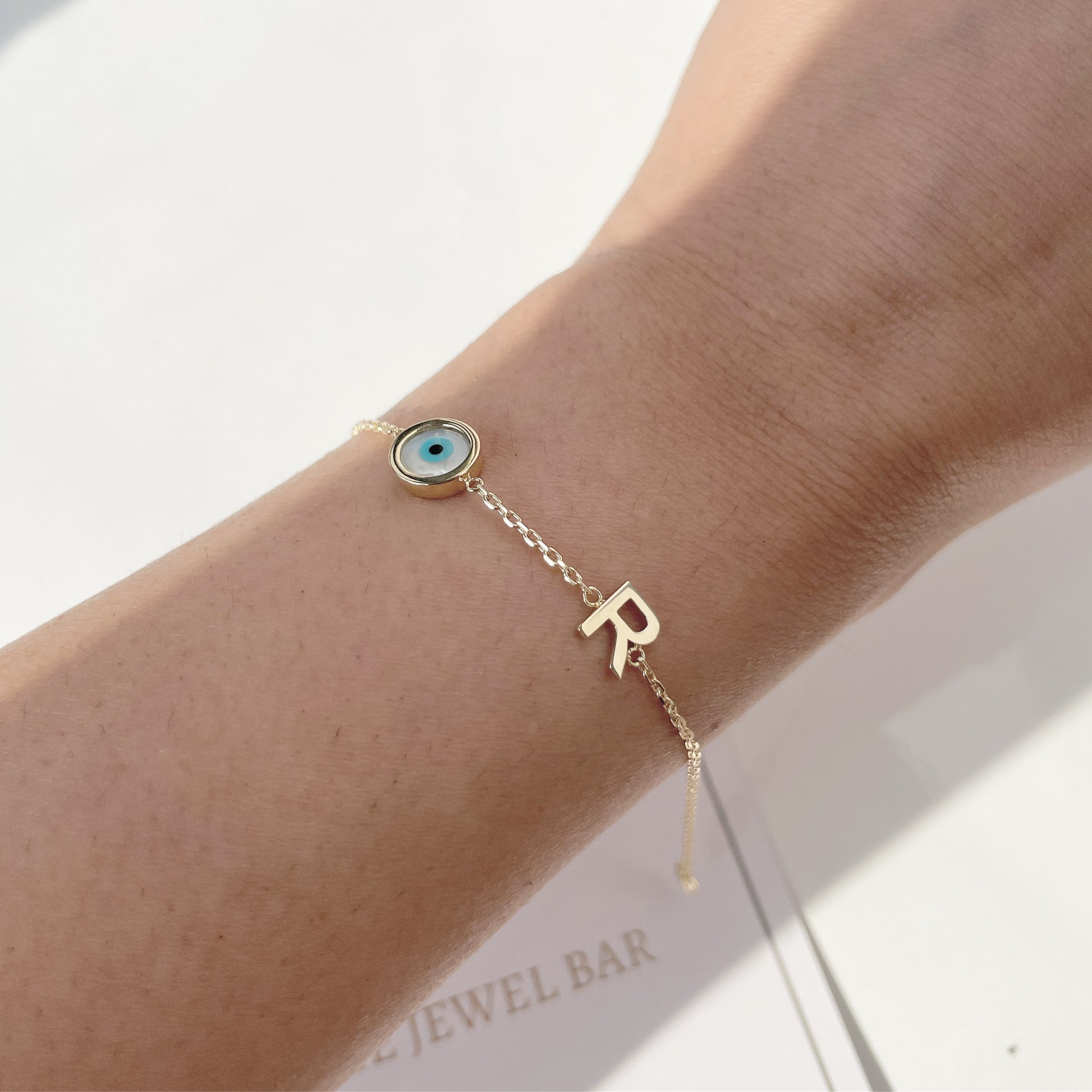 A gold initial bracelet with a bezel set mother of pearl evil eye