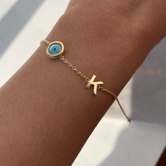 A gold initial bracelet with a bezel set mother of pearl evil eye charm