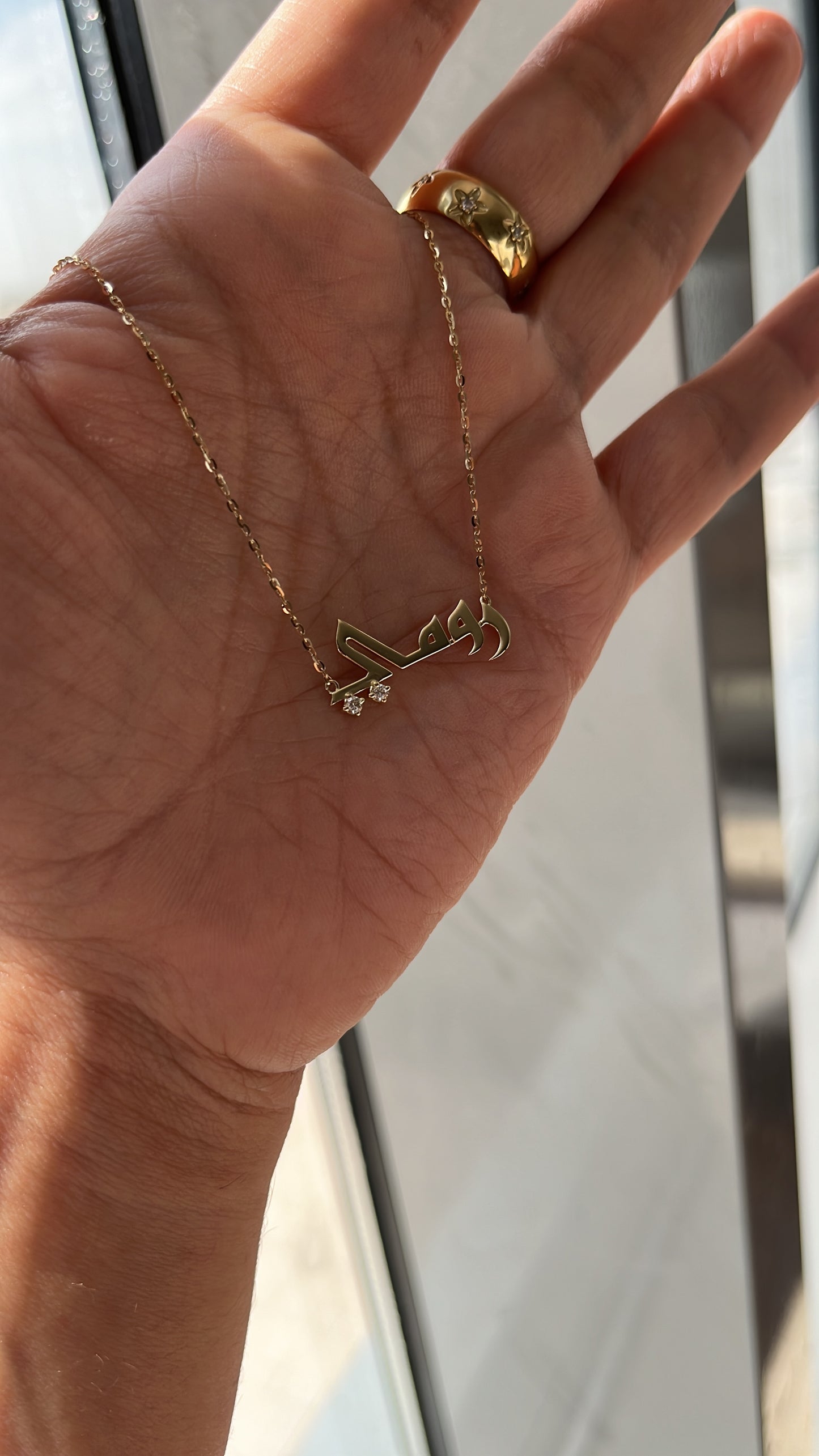 name neckalce in arabic script with diamonds on the dots held up in a hand